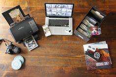 an open laptop computer sitting on top of a wooden table next to other electronics and books