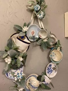 a wreath made out of tea cups and saucers with greenery on the side