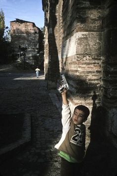 a young boy standing next to a stone wall holding a cell phone in his hand