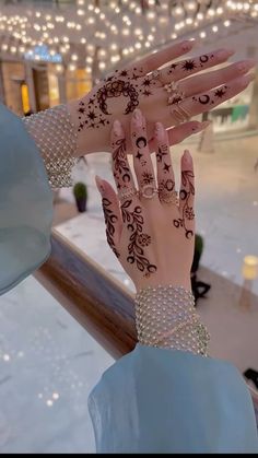 a woman's hands with hennap and jewelry on them in front of a window