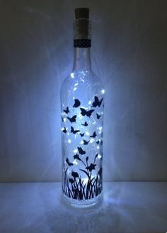 a bottle with some lights in it and grass on the inside is lit up to look like butterflies