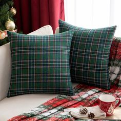 two green plaid pillows sitting on top of a white couch next to a christmas tree