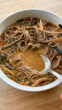 a bowl of noodles with chopsticks in it and someone holding a spoon over the bowl