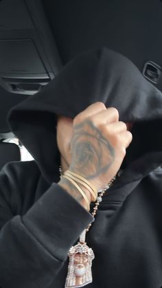 a person wearing a black hoodie with tattoos on their arm and hand in the car