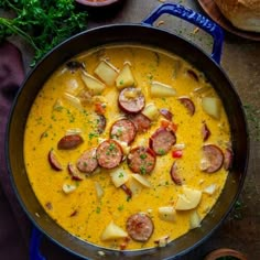 a pan filled with sausage and potatoes on top of a table next to some bread