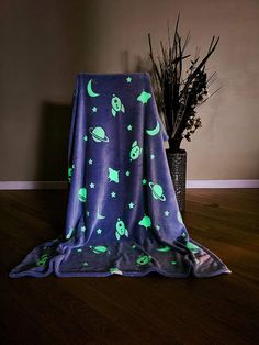 a blanket with glow in the dark stars and planets on it is sitting next to a potted plant