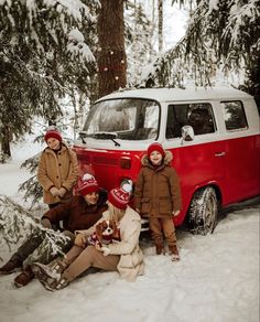 three people are sitting in the snow next to a red and white vw van