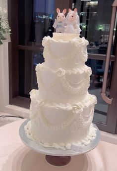 a three tiered white wedding cake with bunnies on the top and frosting