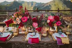 the table is set with red and pink flowers in vases, napkins, and place settings