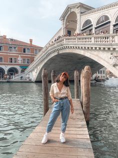 a woman standing on a dock in front of a bridge with gondola bridges