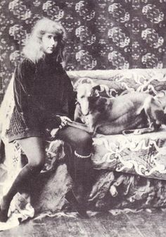 an old black and white photo of a woman sitting on a bed with two dogs