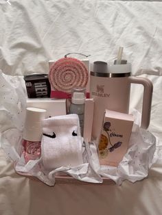 a basket filled with personal care items on top of a white sheet covered bed next to a cup