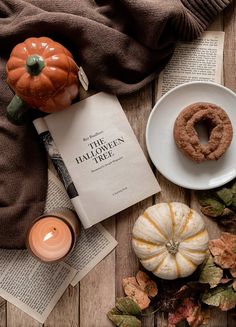 a table topped with books and pumpkins next to a plate filled with doughnuts