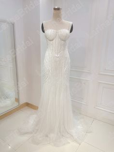 a white wedding dress on display in front of a mirror with an open back and beading