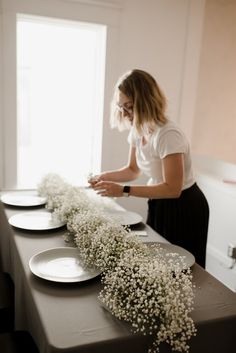 a woman standing at a table with plates and flowers in front of her on it