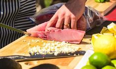 a person cutting up meat on top of a wooden table next to lemons and limes