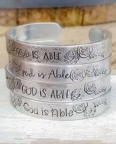 "This listing is for a custom, hand stamped 3/8\" wide aluminum cuff stamped with \"God is able\" in your choice of font and finish. See photos for details. Bracelet is 3/8\" wide, 6\" long before bending, and is lightweight, but durable. 12 gauge is sturdy enough for everyday wear. You can slightly bend to fit your wrist better, but it will still slide off and on easily! Each cuff fits small to average sized wrists best. Flowers can be omitted upon request. Convo me with questions! Made with lo Verse Bracelet, God Is Able, Bible Verse Bracelet, Ephesians 3 20, Nail Buffer Block, Scripture Jewelry, Necklace Length Guide, Best Flowers, 12 Gauge