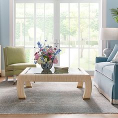 a living room filled with furniture and flowers on top of a coffee table in front of a window