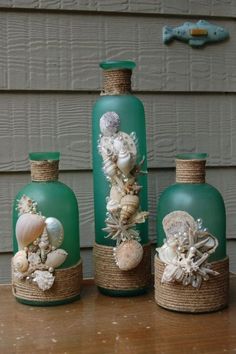 three green glass bottles with sea shells in them