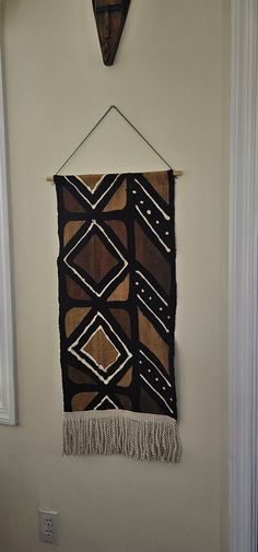 a black and brown wall hanging on the side of a white wall next to a window