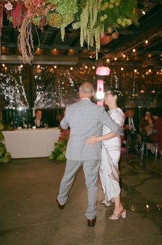 a bride and groom dance together at their wedding reception in an indoor venue with hanging flowers