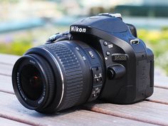 a nikon camera sitting on top of a wooden table next to a flower garden