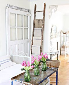 a table with flowers in vases on top of it next to a chair and window