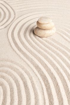 a rock sitting on top of a white sand covered ground with wavy lines in the background