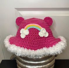 a pink crocheted hat with a rainbow on the top and white fluffy trim