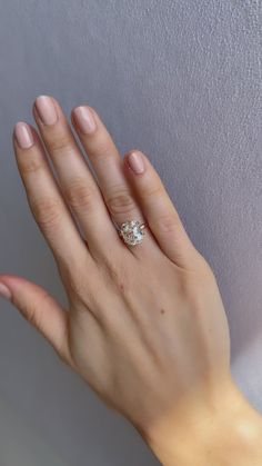 a woman's hand with a diamond ring on her left hand, against a white wall