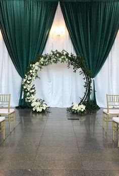 a wedding ceremony set up with green drapes and white flowers on the floor, along with gold chairs