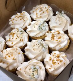 cupcakes with white frosting and gold sprinkles in a box