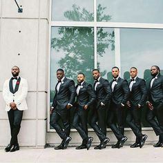 a group of men in tuxedos standing next to a building with their legs crossed