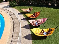 three people laying in hammocks next to a swimming pool on the grass,