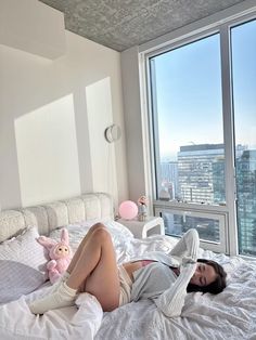 a woman laying on top of a white bed in a bedroom next to a large window