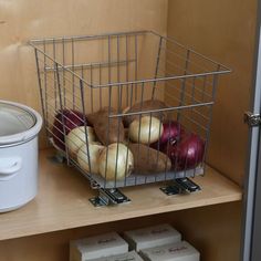 a metal basket filled with apples and onions on top of a wooden shelf next to an ice bucket