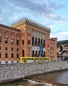 an old building with a yellow train on the tracks next to it and water running underneath