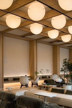 a room with couches, tables and lamps on the ceiling is lit by round lights