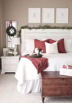 a white bed topped with pillows and blankets next to a wooden trunk filled with presents