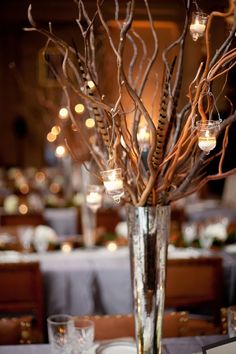 a vase filled with branches and candles on top of a table covered in white linens