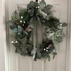 a wreath hanging on the front door with greenery and pine cones attached to it