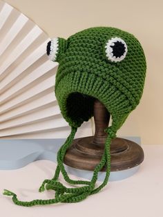 a green knitted hat with eyes on top of a wooden stand next to a fan