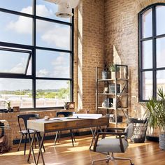 an office space with large windows and wooden flooring, along with a desk in the middle