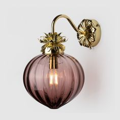 a wall light with a pink glass ball and gold metal accents on the arm, against a white background