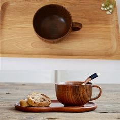 there is a wooden tray with two cups on it and one has a spoon in it