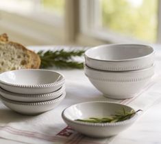 a table topped with white bowls and plates filled with food next to a slice of bread