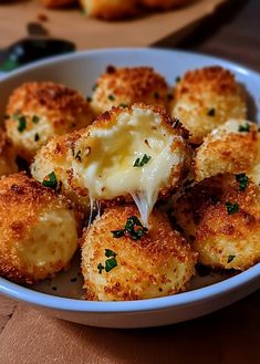 a white bowl filled with cheese covered tater tots on top of a wooden table