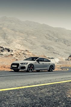 a silver car driving down the road near mountains