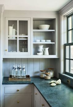 a kitchen with white cabinets and green counter tops, along with dishes on the shelves