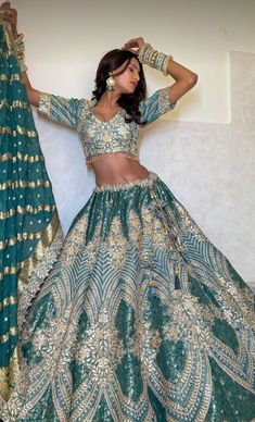 a woman in a green and gold lehenga with her arms behind her head